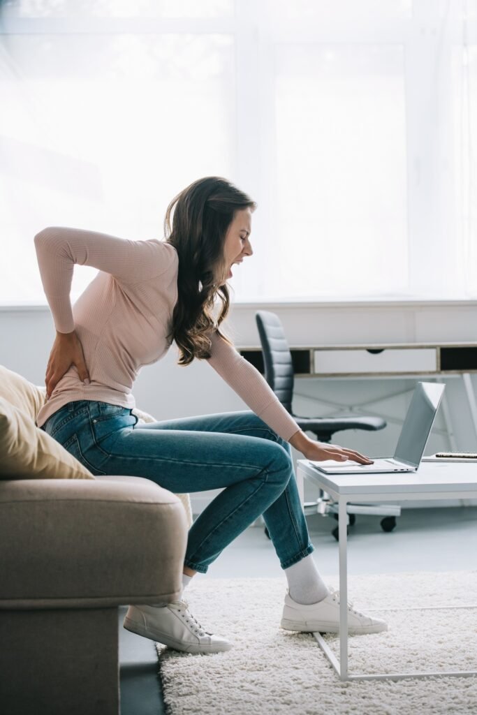 young woman suffering from back pain while using laptop at home